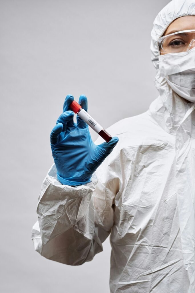 Scientist in PPE holding a blood test sample tube in a laboratory setting.